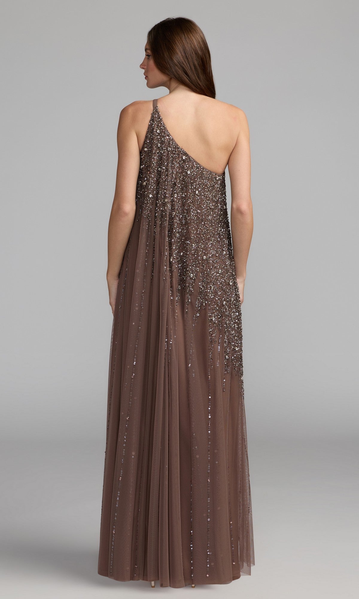 A woman faces away, wearing the Mac Duggal 9224 one-shoulder long formal dress—a floor-length brown gown with sequins and a sheer overlay—ideal for special occasions.